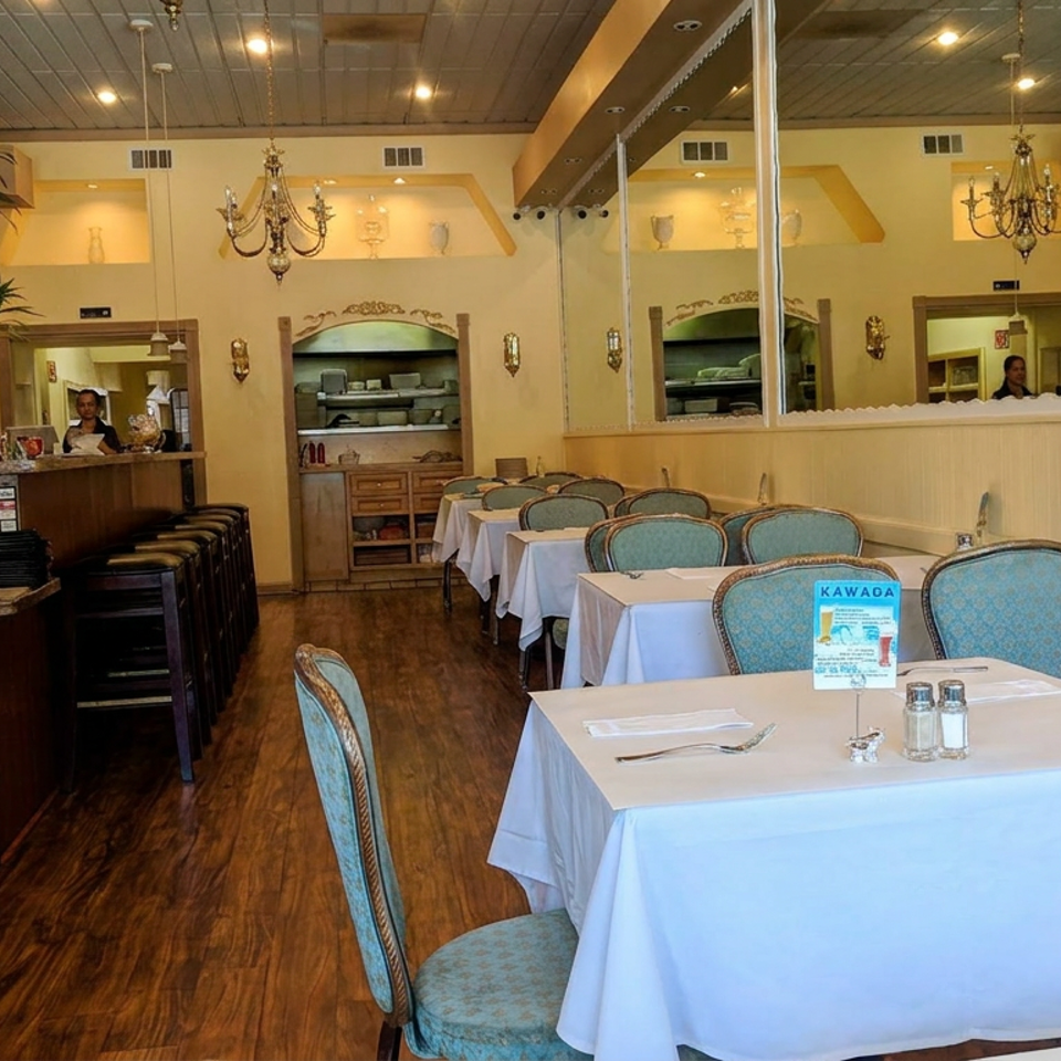 Elegant restaurant dining room with white tablecloths, blue upholstered chairs, chandeliers, mirrored walls, and a bar.